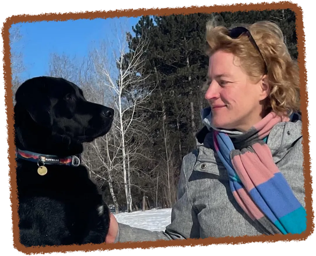 Clémentine Reynaud de profil avec un foulard coloré regarde un grand chien noir dans un paysage hivernal enneigé.
