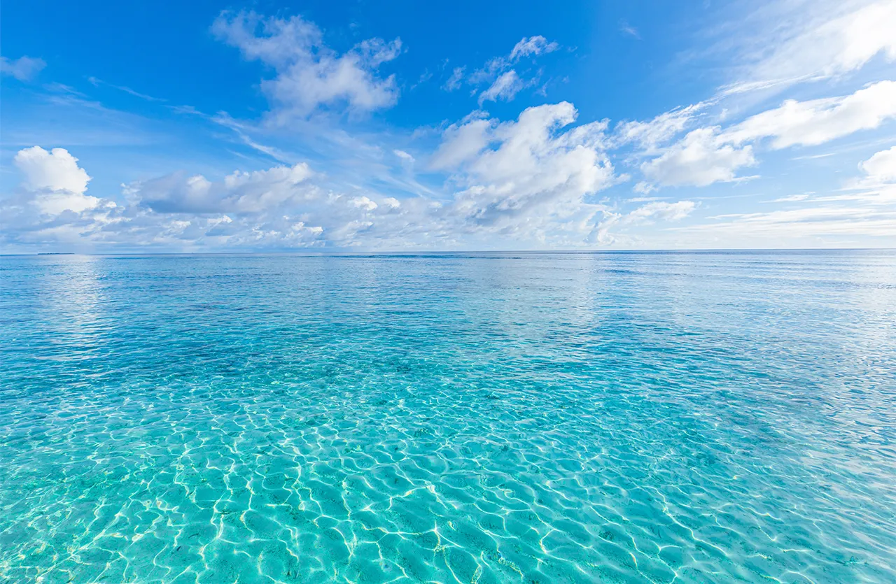 Mer calme à l’horizon sous un ciel bleu avec plusieurs nuages blancs dispersés.
